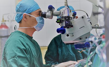 Surgeon wearing scrubs looking into eye machine 